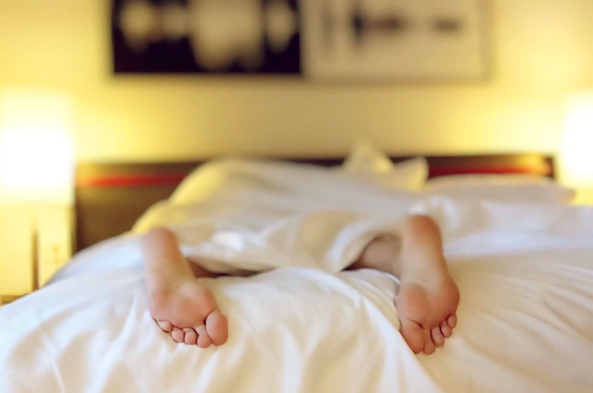 person laying face down in bed under a sheet