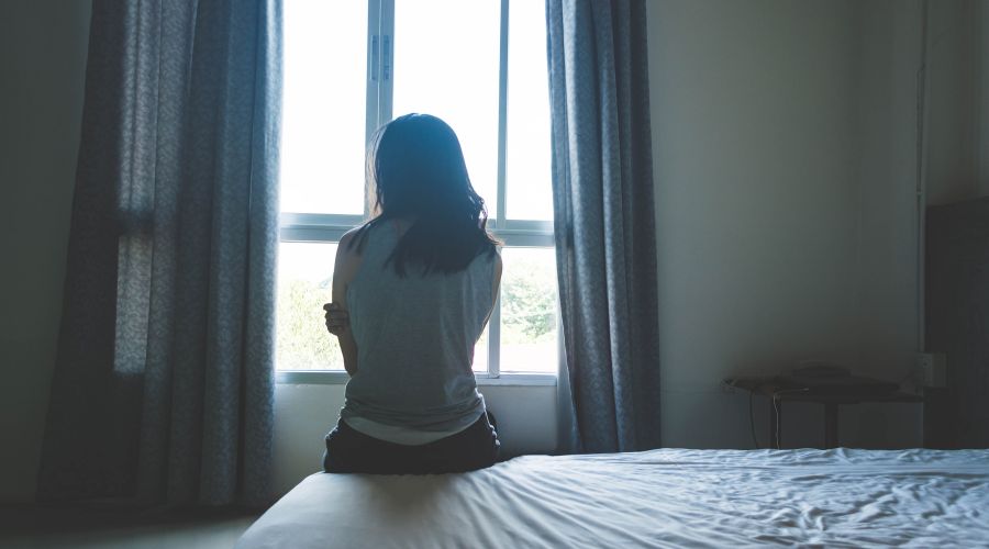 Woman sitting at the edge of her bed looking outside