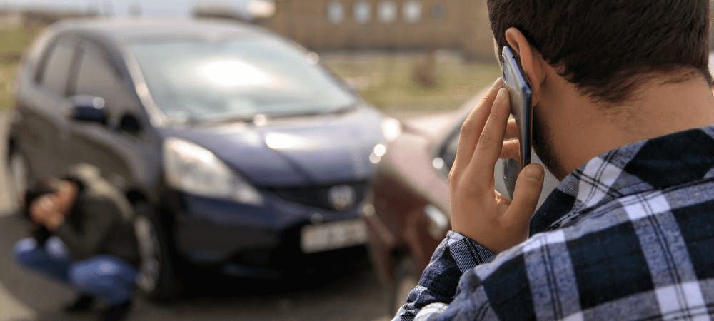 Man on phone in foreground with damaged car in background